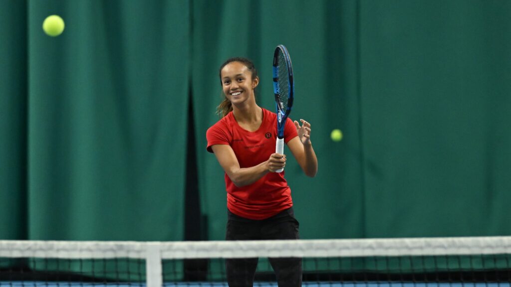 NCAA player Bianca Jolie Fernandez smiles as she follows through on a forehand.