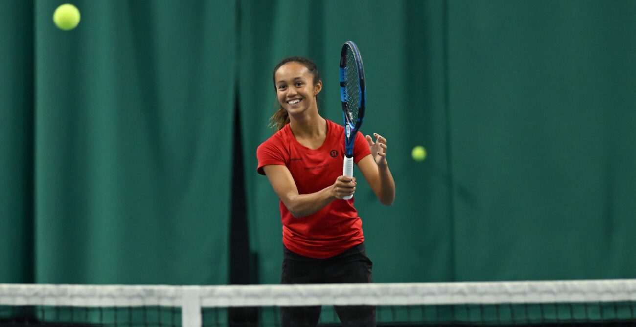 NCAA player Bianca Jolie Fernandez smiles as she follows through on a forehand.