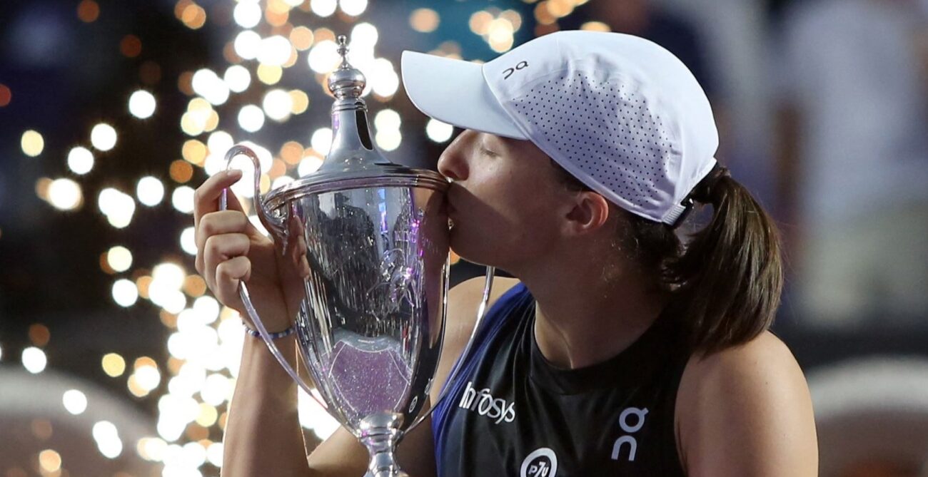 Iga Swiatek kisses the WTA Finals trophy.