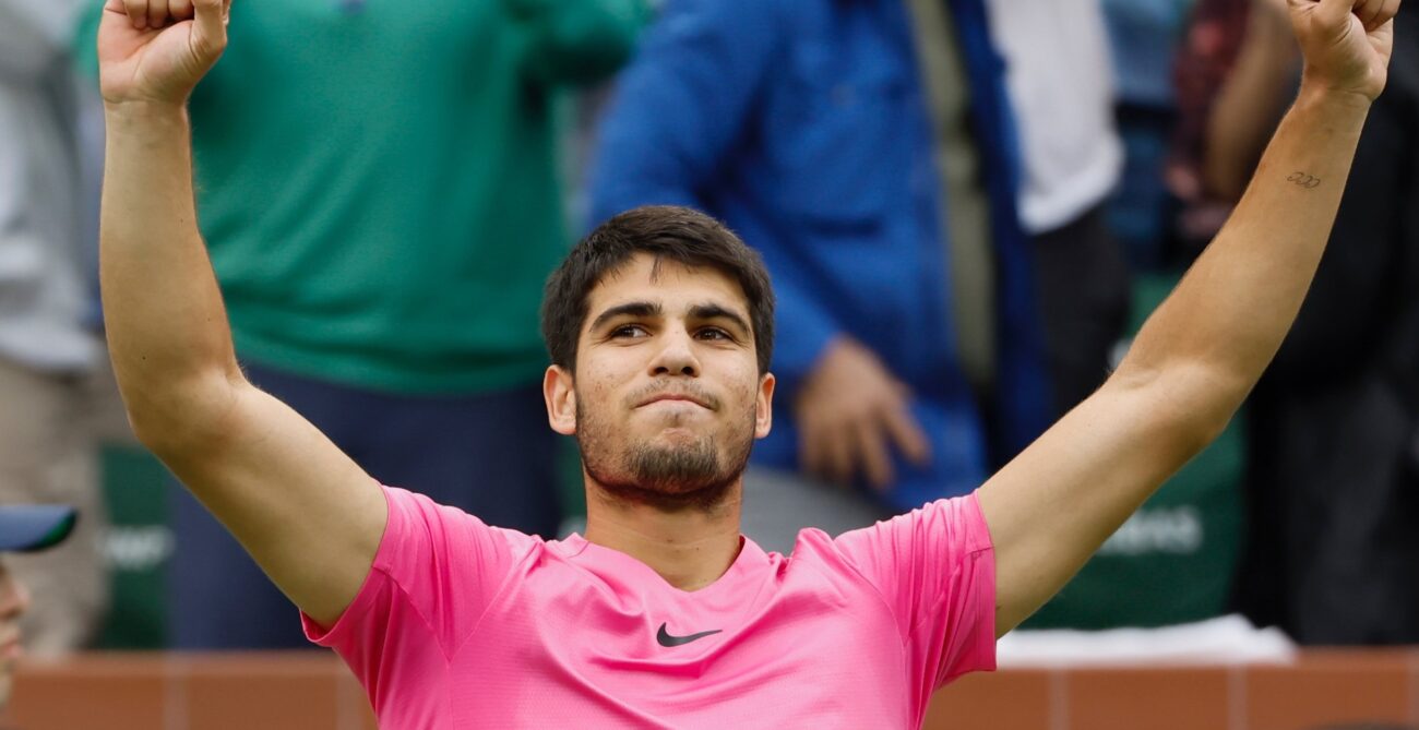 Carlos Alcaraz raises his fists above his head in triumph.