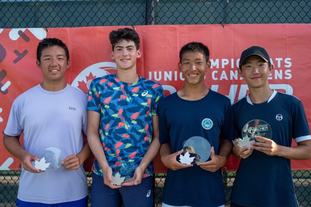 Four boys hold their trophies in front of the Fischer Junior Nationals sign.