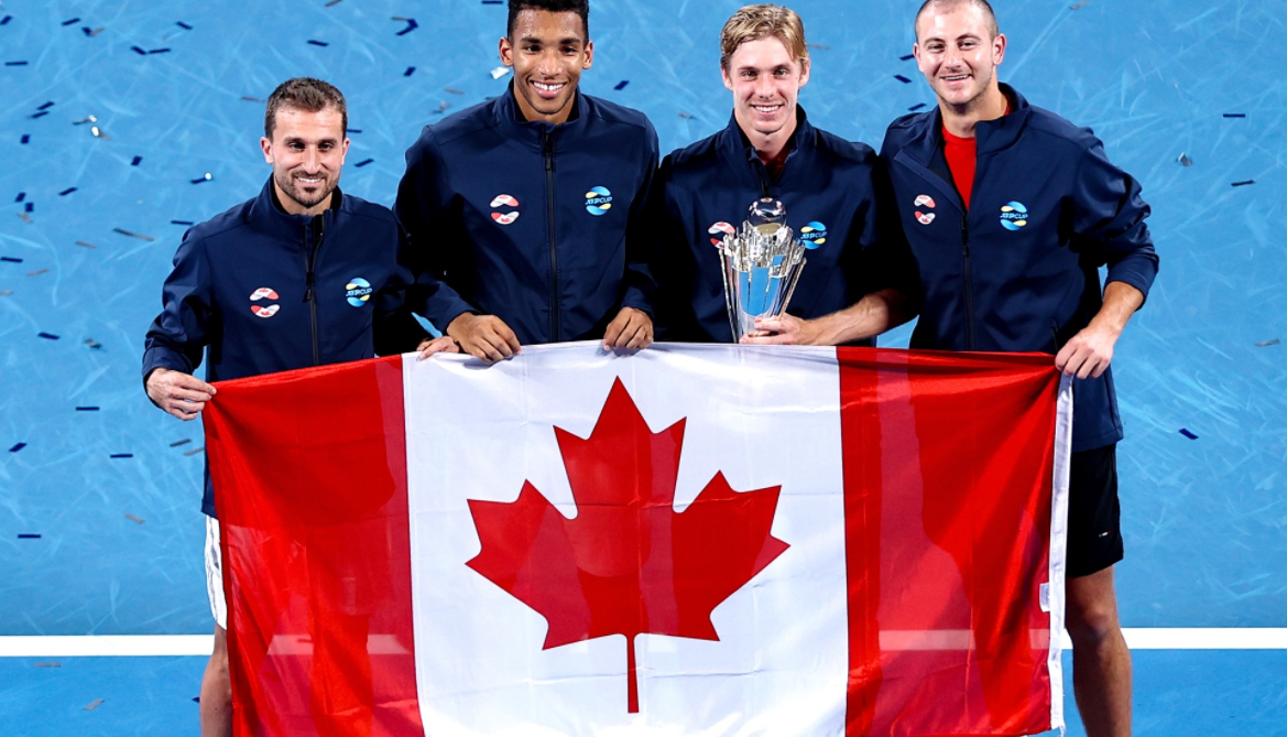 Steven Diez, Felix Auger-Aliassime, Denis Shapovalov and Brayden Schnur hold up the Canadian flag standing on the court while Shapovalov holds the ATP Cup trophy.