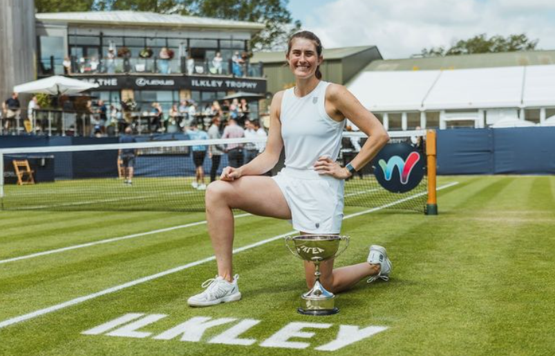 Rebecca Marino kneels on the grass court at Ilkley behind the trophy. She plays this week in qualifying at Wimbledon.